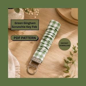 May include: A green and white gingham fabric scrunchie key fob with a silver metal hardware clamp and a circular split ring. The image includes text that reads Green Gingham Scrunchie Key Fob, PDF PATTERN, and INSTANT DOWNLOAD.