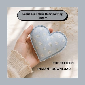 May include: A light blue fabric heart with a white floral pattern and scalloped edges. The text Scalloped Fabric Heart Sewing Pattern, PDF PATTERN, and INSTANT DOWNLOAD are visible. The heart is held in a hand wearing a cream-colored sleeve.