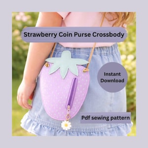 May include: A light purple strawberry-shaped coin purse crossbody bag with a light green leaf top and a daisy charm. The bag has a zipper and a long strap. Text on the image says "Strawberry Coin Purse Crossbody", "Instant Download", and "Pdf sewing pattern".