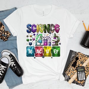 Pode incluir: Camiseta branca com um gráfico colorido que diz "SCIENCE TEACHER". O design inclui imagens relacionadas à ciência, como um microscópio, béqueres e estruturas moleculares. A camisa é combinada com jeans azuis e tênis pretos.