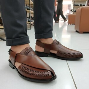 May include: Brown leather sandals with woven and smooth textures. The sandals have a strap around the ankle and a buckle closure. The shoes are on a black sole.