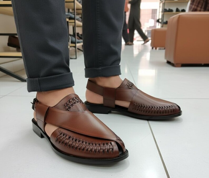May include: Brown leather sandals with woven and smooth textures. The sandals have a strap around the ankle and a buckle closure. The shoes are on a black sole.