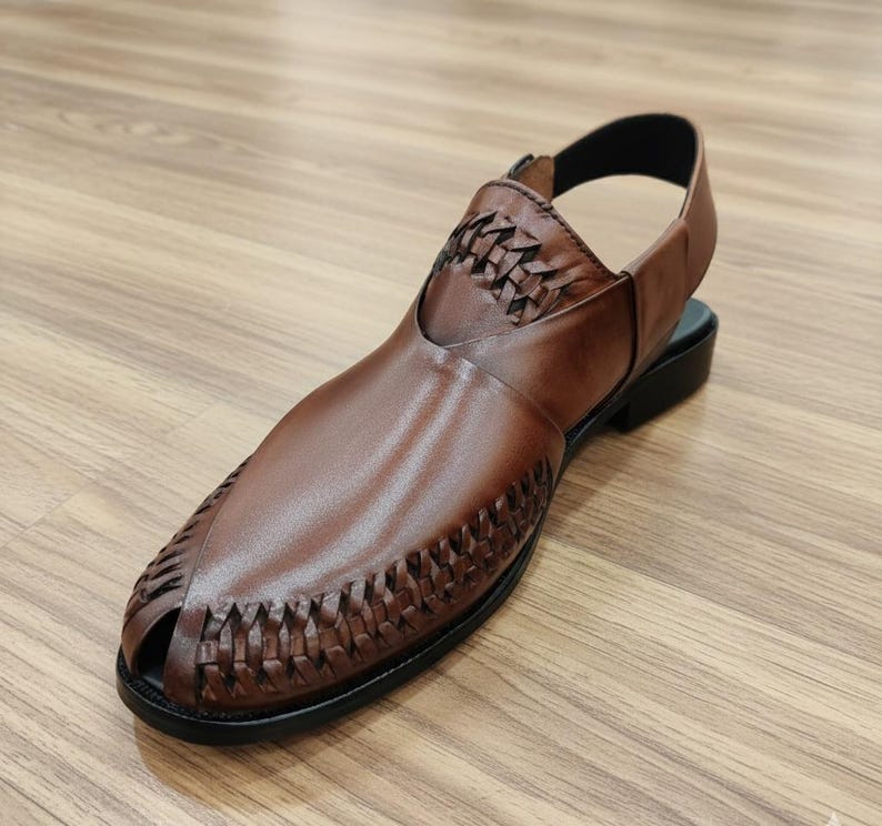 May include: Brown leather sandal with a woven design on the vamp and upper. The sandal has a slingback strap and a black sole. The open-toe design and the woven details give the sandal a unique look. The sandal is made of leather.