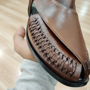 May include: Brown leather sandal with woven detailing on the vamp. The open-toe shoe has a smooth leather upper and a black sole. The sandal is designed for comfort and style, suitable for casual wear.