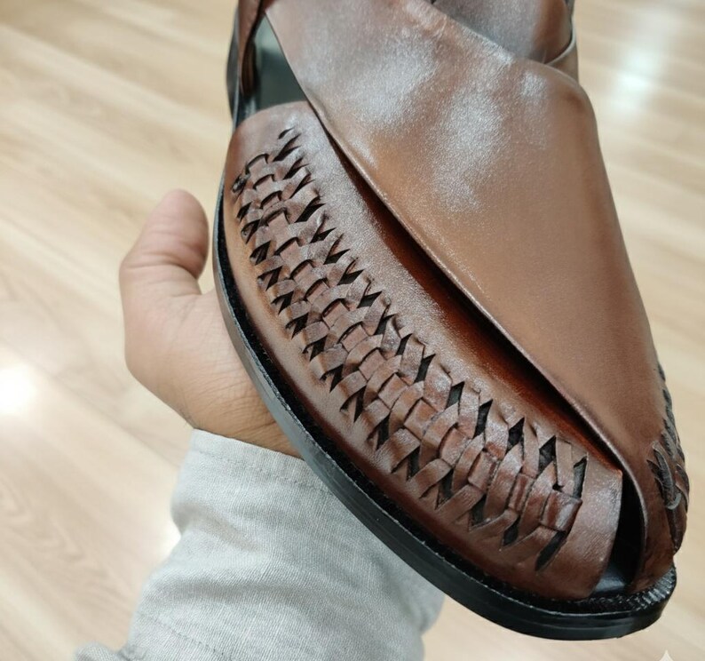 May include: Brown leather sandal with woven detailing on the vamp. The open-toe shoe has a smooth leather upper and a black sole. The sandal is designed for comfort and style, suitable for casual wear.
