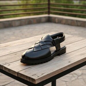 May include: Black leather sandal with a woven vamp design. The sandal features a thick, lug sole and an adjustable ankle strap. The shoe is displayed on a wooden table, showcasing its construction and style.