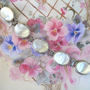 May include: A silver-toned link bracelet featuring five oval-shaped, iridescent mother-of-pearl cabochons. Each stone is set within a textured metal frame, connected by small rectangular links, and secured with a metal clasp at the end.