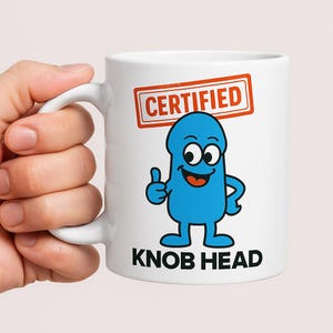 May include: White ceramic mug with a cartoon blue character giving a thumbs-up. The mug has the words "CERTIFIED" and "KNOB HEAD" in red and black text. The mug has a white handle.