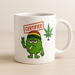 May include: White ceramic mug with a green cartoon character smoking a cigarette, giving a peace sign, and a "CERTIFIED" stamp. A cannabis leaf with a face is also on the mug.