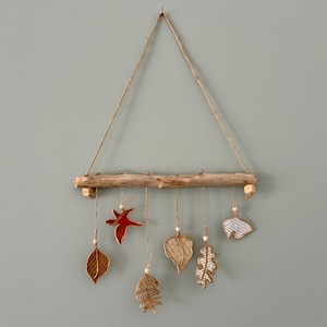 May include: A handmade wall hanging featuring a driftwood branch with hanging leaf-shaped ornaments. The leaves are made of various materials, including red ceramic and paper, and are suspended by twine. A natural, rustic home decor item.