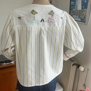 Può includere: Una tazza di ceramica bianca con manico nero e la scritta "But First, Coffee" in nero, con un carattere a mano. La tazza è su una superficie bianca.