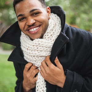 May include: A man wearing a black peacoat with a white knit scarf. He is smiling and looking at the camera.