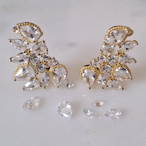 Puede incluir: Un par de pendientes de oro con un racimo de cristales transparentes en forma de pera. También hay cinco cristales sueltos en la superficie.