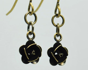 May include: A pair of gold-toned earrings with black flower-shaped charms. The earrings have a simple chain design and a hook closure.