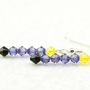 Puede incluir: Pendientes de plata con un colgante de cuentas con cuentas de cristal negras, moradas y amarillas.