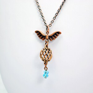 May include: A copper necklace with a winged pendant, a cage-like charm, and two blue crystal beads.