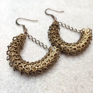 May include: A pair of gold-toned hoop earrings with a delicate, textured design. The earrings are made of metal and have a chain link drop.