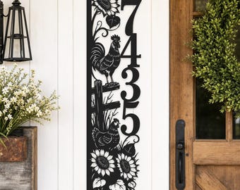 Puede incluir: Un letrero vertical de metal negro para número de casa con los dígitos 7435. El diseño incluye un gallo sobre una cerca, una gallina debajo y girasoles en la parte superior e inferior. El letrero tiene un estilo recortado y está en una pared blanca.