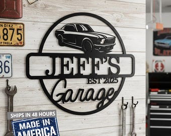 May include: Black metal garage sign with a classic car silhouette, the name "JEFF'S Garage" and "EST 2025". The sign is mounted on a wooden wall with vintage license plates and tools. A "Made in America" sticker is visible.