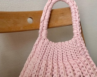May include: A pink crocheted tote bag with a single handle. The bag is made with a thick yarn and has a slightly textured surface.
