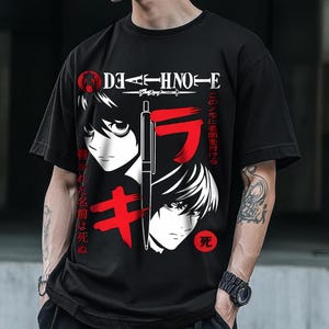 May include: Black t-shirt featuring a graphic design with Japanese text and anime-style illustrations. The design includes the text "DAA-HNO-E" and other Japanese characters in red and white. A pen is also featured in the design.