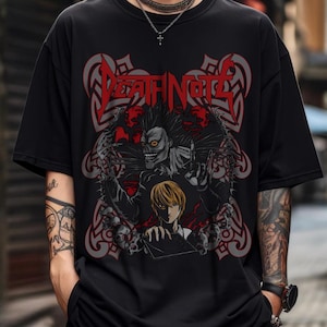 May include: Black t-shirt featuring a graphic design with the text "Death Note" in red, stylized lettering. The design includes a skeletal figure, a character with blonde hair, and skull imagery. The shirt is a short-sleeved crew neck.
