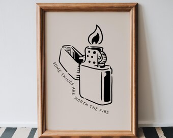 May include: A framed print featuring a black and white illustration of a lighter with a flame. The text "SOME THINGS ARE WORTH THE FIRE" is printed in a circular pattern around the lighter. The frame is a light brown color.