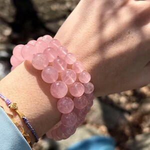 May include: A pink rose quartz beaded bracelet with multiple strands of round beads. The bracelet is worn on a person's wrist.
