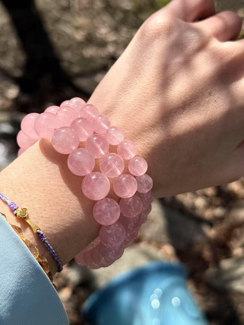 May include: A pink rose quartz beaded bracelet with multiple strands of round beads. The bracelet is worn on a person's wrist.