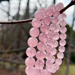 May include: A pink rose quartz beaded bracelet with multiple strands of beads. The bracelet is hanging from a branch.