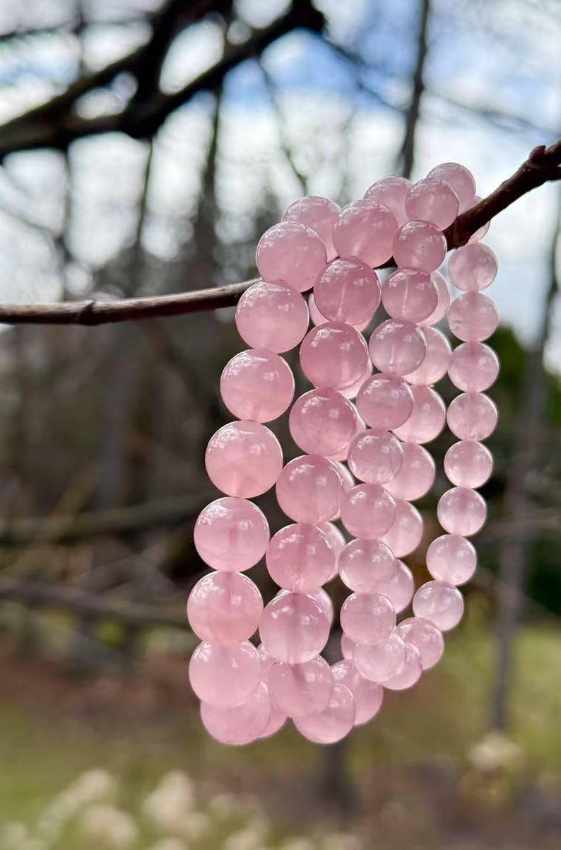 May include: A pink rose quartz beaded bracelet with multiple strands of beads. The bracelet is hanging from a branch.