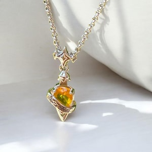 Könnte beinhalten: Eine goldfarbene Halskette mit einem Anhänger in Form einer Zaubertrankflasche. Die Flasche enthält gelbe und grüne Flüssigkeit und ist von einem Band mit den Worten "Felix Felicis" umgeben. Die Kette hat einen sternförmigen Akzent.