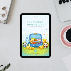May include: A tablet shows a vibrant illustration of a blue lunchbox packed with food, including sandwiches, fruit, and vegetables. The text "LONCHERAS DIVERTIDAS" is at the top. A football, banana, and panda are also shown. The tablet is on a light grey surface.