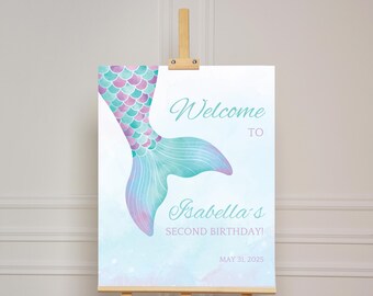 May include: A mermaid-themed welcome sign on an easel. The sign features a watercolor mermaid tail in shades of teal, purple, and pink. Text reads "Welcome to Isabella's SECOND BIRTHDAY!" with the date May 31, 2025.