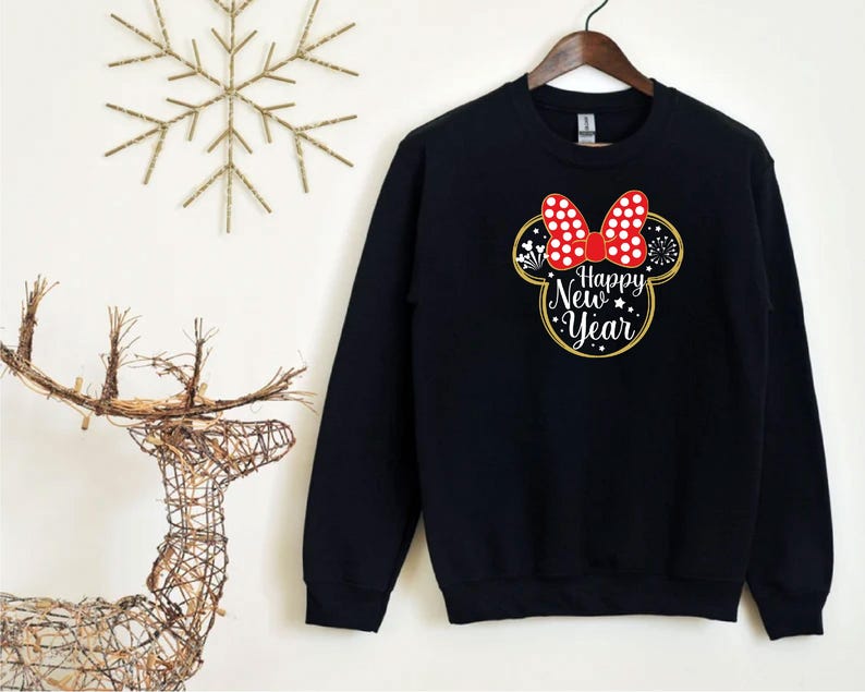 May include: Black sweatshirt featuring a Minnie Mouse-inspired design with a red polka-dot bow and the text "Happy New Year" in white and gold. The design includes fireworks and stars, perfect for holiday celebrations.