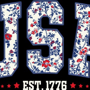 May include: A graphic design featuring the word "USA" in a bold, collegiate-style font, filled with a floral pattern of red and blue flowers on a cream background. Below, the text "EST. 1776" is displayed with red stars on a black background.