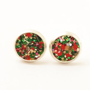 May include: A pair of silver stud earrings with a round, red, green, gold, and pink glitter design.