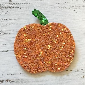 Könnte beinhalten: Eine glitzernde orangefarbene Kürbisdekoration mit einem grünen Glitzerstiel. Der Kürbis ist mit orangefarbenem und goldenem Glitzer bedeckt, was einen funkelnden Effekt erzeugt. Ideal für Herbst- und Halloween-Dekorationen.