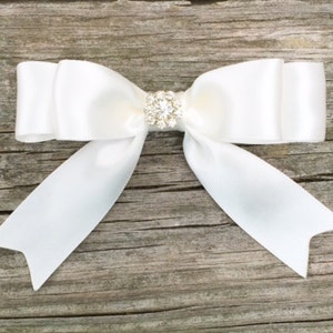 May include: A white satin bow with a clear rhinestone embellishment in the center.