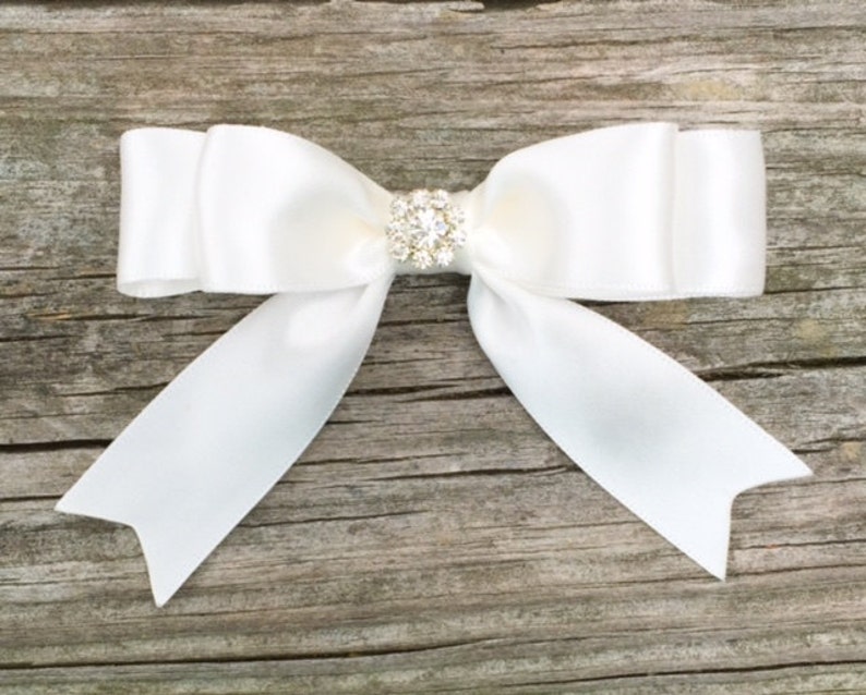 May include: A white satin bow with a clear rhinestone embellishment in the center.
