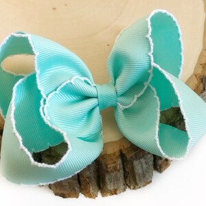 May include: A light blue bow with white scalloped edges. The bow is made of a soft, silky fabric and is perfect for adding a touch of elegance to any outfit.