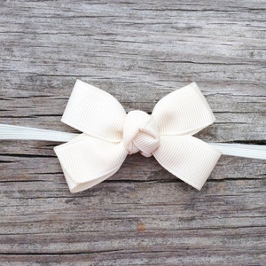 May include: A white satin bow tied with a white ribbon on a weathered wooden surface.