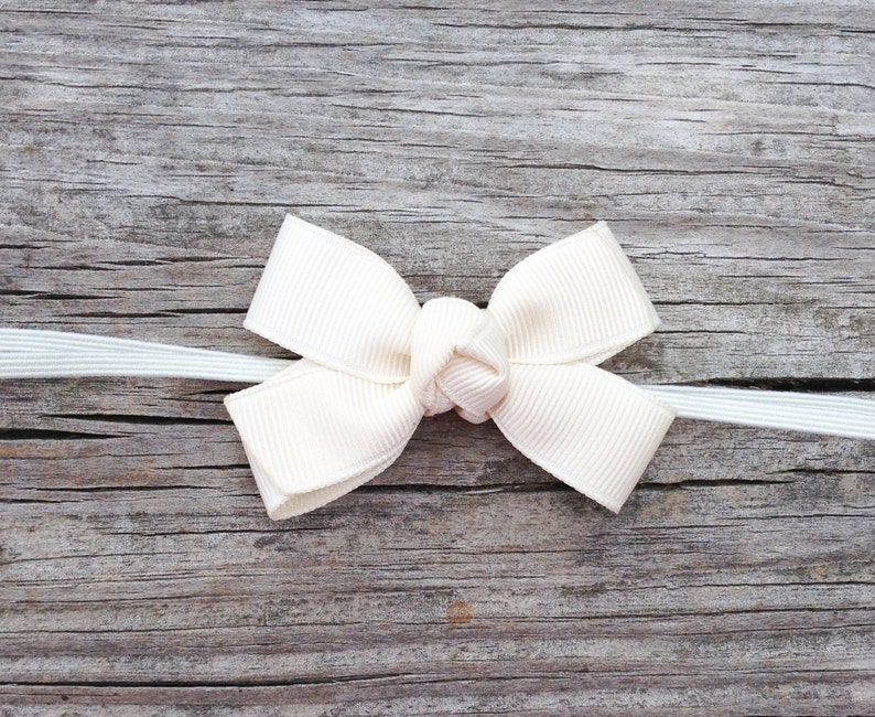 May include: A white satin bow tied with a white ribbon on a weathered wooden surface.