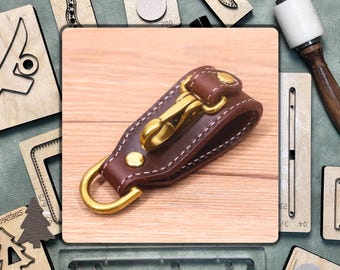 May include: A brown leather key chain with a brass hook and a white stitching detail. The key chain is on a wooden surface.