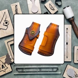 May include: Two handcrafted leather holsters with a brown and tan gradient, featuring decorative stitching and a brass emblem. The holsters are displayed on a white background, surrounded by leatherworking tools and wooden stamps.
