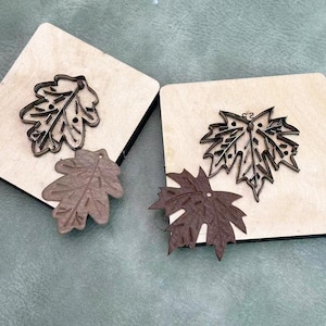 Peut inclure: Deux découpes de feuilles en cuir marron et une découpe de feuille en métal brun foncé sur un bloc de bois. La découpe a une mesure de 6,35 cm. L'autre feuille est de couleur marron clair. Le fond est vert clair.