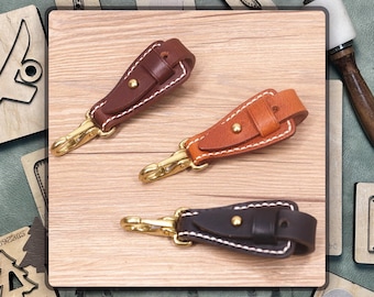 May include: Three leather keychains with brass key rings. The keychains are brown, orange, and black. Each keychain has a stitched design and a small metal rivet.