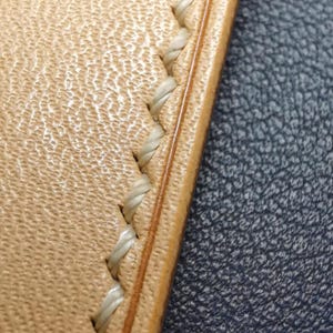 May include: Close-up of a light brown leather strap with a white stitching detail. The stitching is a decorative stitch pattern.