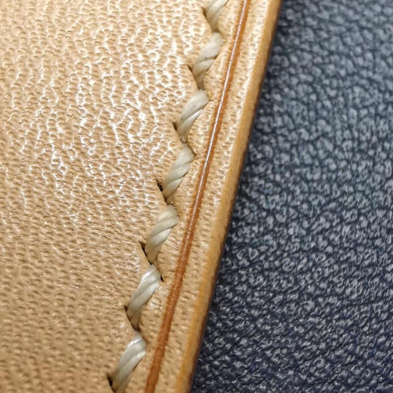May include: Close-up of a light brown leather strap with a white stitching detail. The stitching is a decorative stitch pattern.