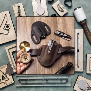Könnte beinhalten: Eine Sammlung von Lederhandwerkzeugen und Zubehör, darunter eine braune Leder-Messerscheide, ein Kompass, ein Klappmesser und verschiedene Holzstanzformen. Die Artikel sind auf einer Holzoberfläche angeordnet.